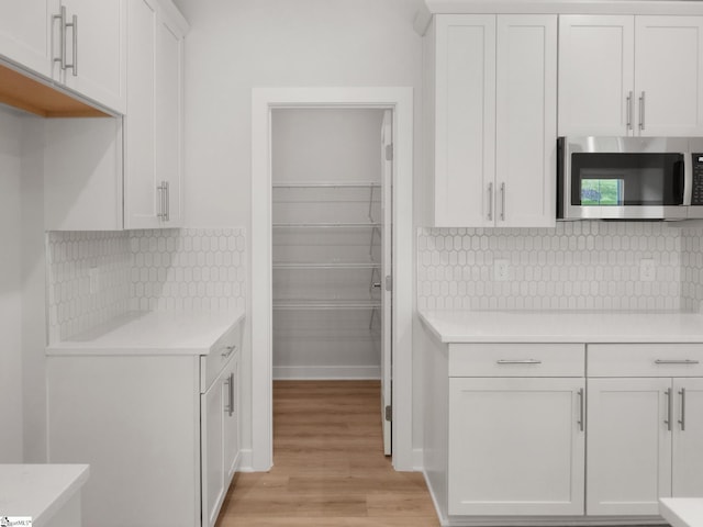 kitchen with white cabinets, light wood-type flooring, and backsplash