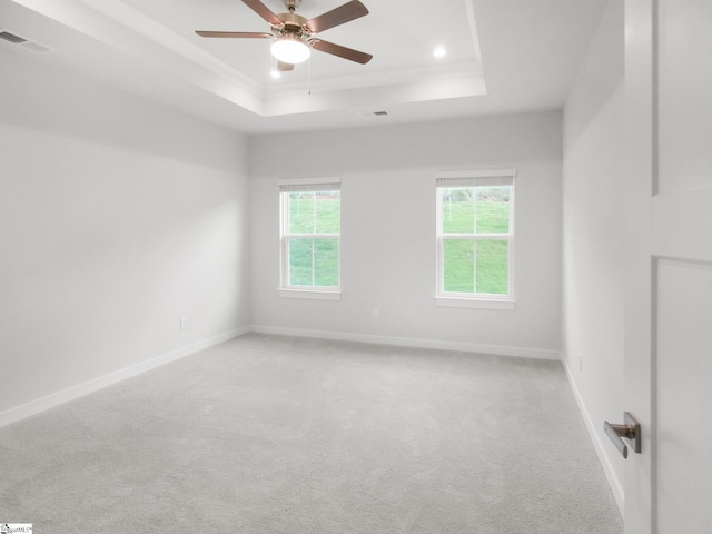 spare room with ceiling fan, light colored carpet, and a tray ceiling