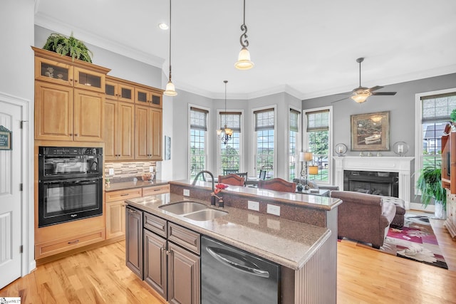 kitchen featuring dishwasher, a kitchen island with sink, sink, black double oven, and light stone countertops