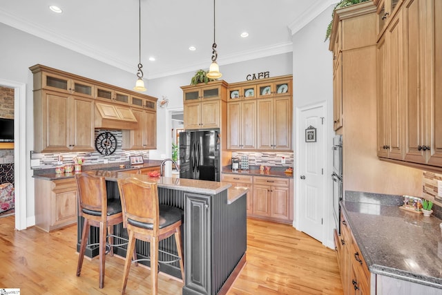 kitchen with black refrigerator, a kitchen bar, pendant lighting, dark stone countertops, and an island with sink