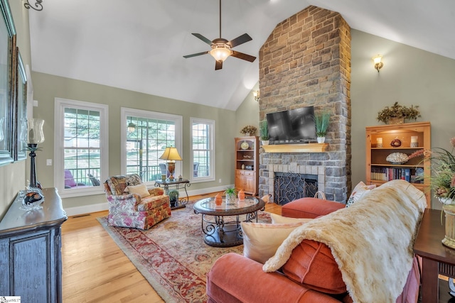 living room featuring light wood-type flooring, high vaulted ceiling, a brick fireplace, and ceiling fan