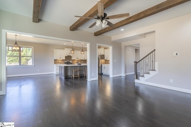 unfurnished living room featuring beamed ceiling, ceiling fan with notable chandelier, and dark hardwood / wood-style floors