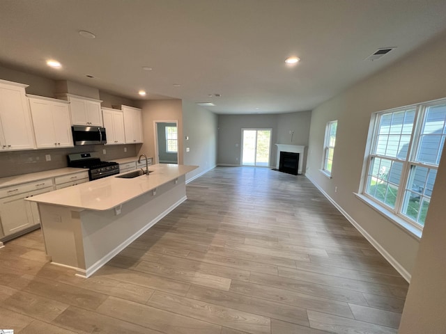 kitchen with sink, a kitchen island with sink, white cabinetry, stainless steel appliances, and light wood-type flooring