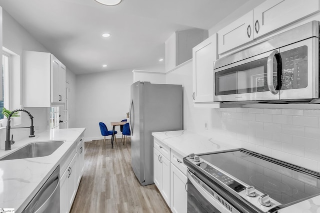 kitchen with white cabinets, stainless steel appliances, light stone countertops, and sink