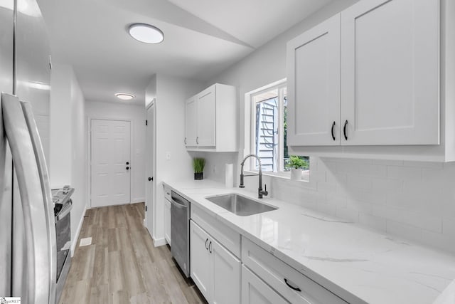 kitchen with appliances with stainless steel finishes, light stone counters, sink, light hardwood / wood-style flooring, and white cabinetry