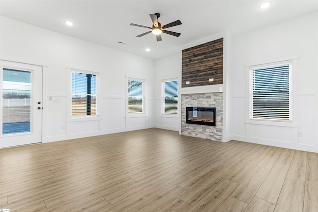 unfurnished living room featuring light hardwood / wood-style floors, a stone fireplace, and ceiling fan