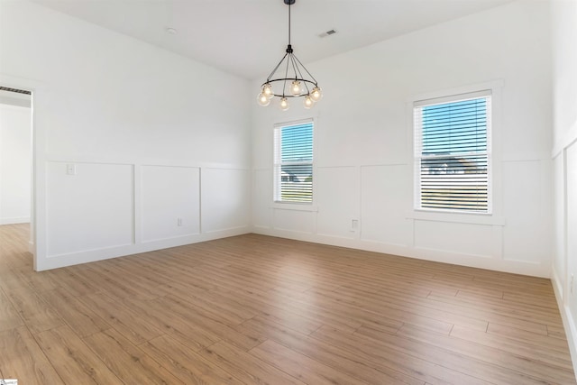 spare room featuring light wood-type flooring and a notable chandelier