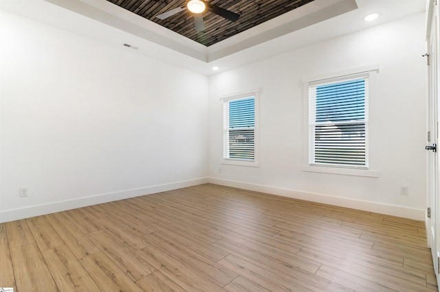 empty room with a tray ceiling, ceiling fan, and light hardwood / wood-style floors