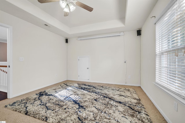 carpeted spare room with a raised ceiling and ceiling fan