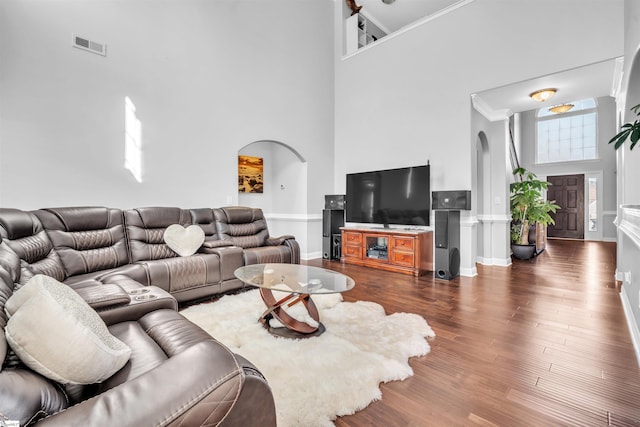 living room featuring dark hardwood / wood-style flooring, a towering ceiling, and ornamental molding