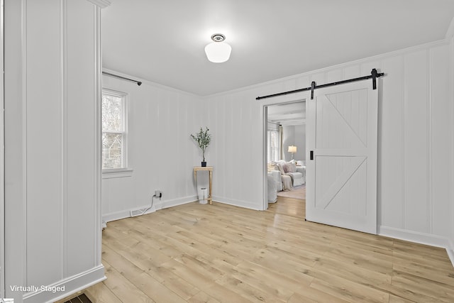 unfurnished room featuring ornamental molding, light wood-type flooring, and a barn door