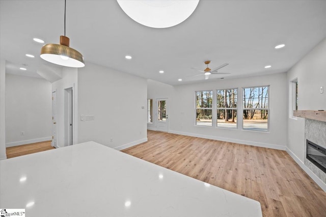 interior space with a tiled fireplace, ceiling fan, and light wood-type flooring