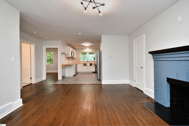 unfurnished living room with a brick fireplace, dark wood-type flooring, and sink