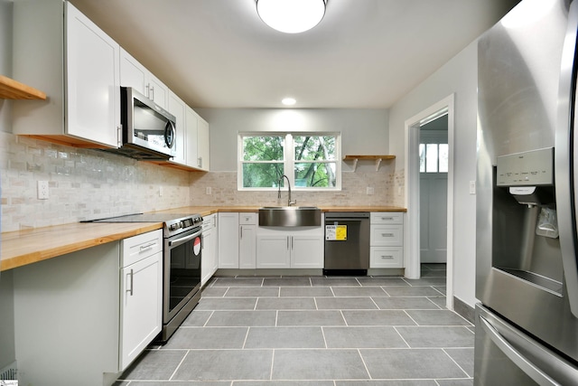 kitchen featuring stainless steel appliances, butcher block countertops, sink, white cabinetry, and backsplash