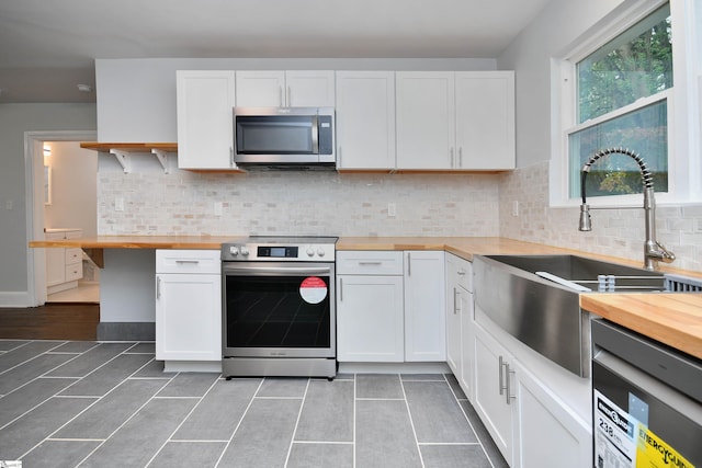 kitchen with wooden counters, stainless steel appliances, sink, and white cabinetry