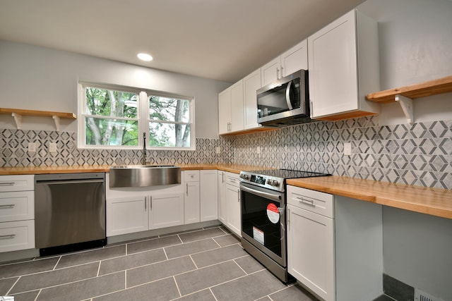 kitchen with wooden counters, dark tile patterned flooring, white cabinetry, appliances with stainless steel finishes, and sink