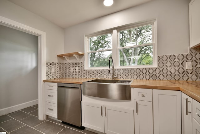 kitchen with stainless steel dishwasher, dark tile patterned floors, butcher block countertops, white cabinets, and sink