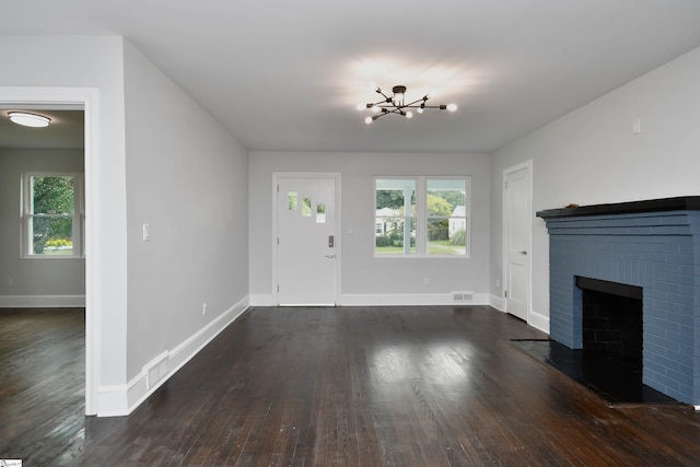 unfurnished living room with dark hardwood / wood-style flooring, a brick fireplace, an inviting chandelier, and a wealth of natural light