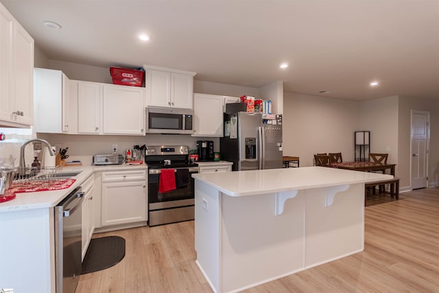 kitchen with stainless steel appliances, sink, white cabinets, a center island, and light hardwood / wood-style flooring