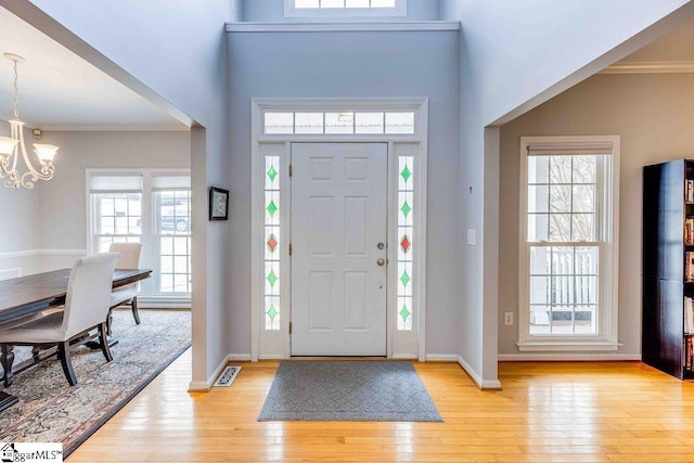 foyer entrance with a towering ceiling, light wood-type flooring, an inviting chandelier, and crown molding