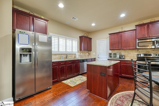 kitchen featuring stainless steel appliances, sink, dark hardwood / wood-style floors, light stone countertops, and a kitchen island