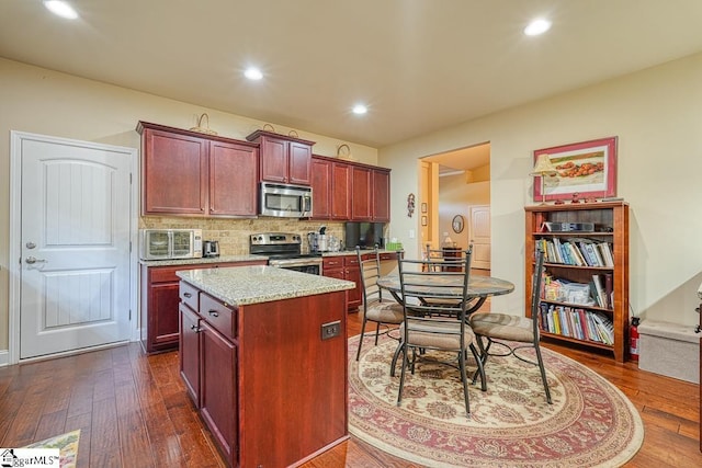 kitchen with light stone counters, tasteful backsplash, a kitchen island, dark hardwood / wood-style flooring, and appliances with stainless steel finishes