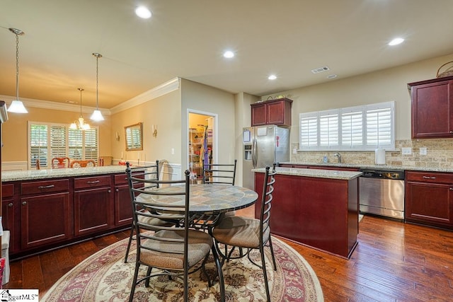 kitchen with appliances with stainless steel finishes, hanging light fixtures, light stone countertops, and dark wood-type flooring