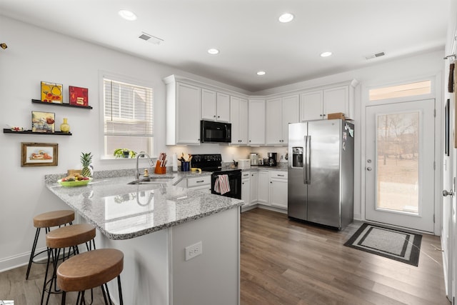 kitchen with kitchen peninsula, light stone countertops, black appliances, white cabinetry, and sink