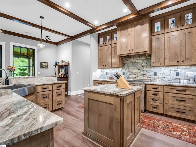 kitchen with light stone counters, light hardwood / wood-style flooring, pendant lighting, a kitchen island, and sink