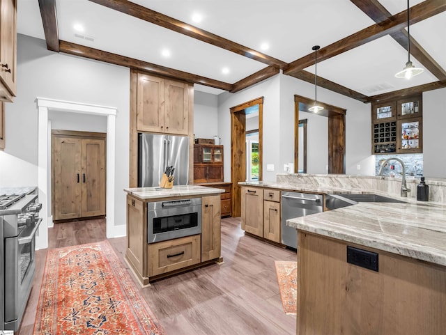 kitchen with high end appliances, decorative light fixtures, light brown cabinetry, light wood-type flooring, and sink