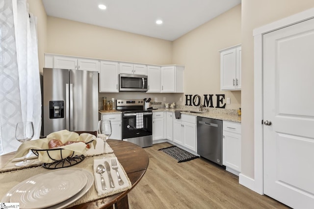 kitchen featuring stainless steel appliances, sink, white cabinets, light stone counters, and light wood-type flooring