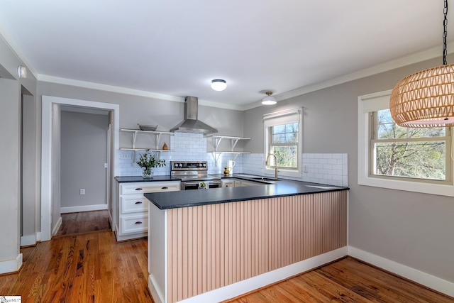 kitchen with wood-type flooring, kitchen peninsula, stainless steel range with electric stovetop, white cabinets, and wall chimney range hood