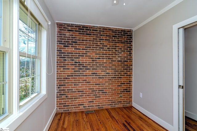 empty room featuring ornamental molding, dark wood-type flooring, and brick wall