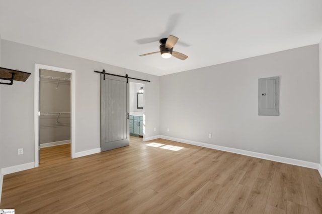 unfurnished bedroom with a spacious closet, electric panel, a closet, a barn door, and ceiling fan