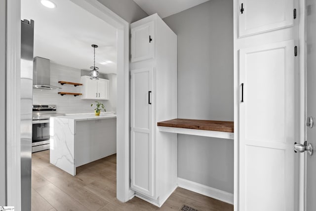 kitchen featuring hanging light fixtures, wall chimney range hood, light hardwood / wood-style floors, white cabinetry, and stainless steel range with electric stovetop