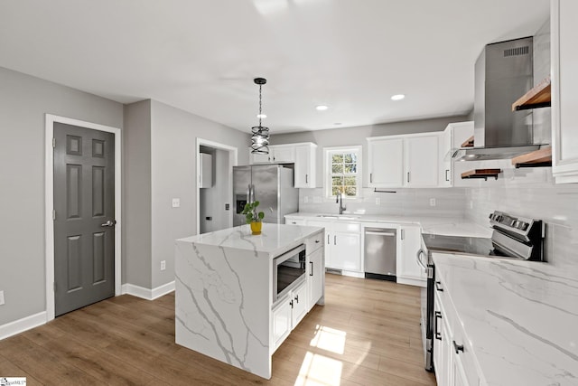 kitchen featuring stainless steel appliances, a center island, white cabinets, wall chimney range hood, and decorative light fixtures