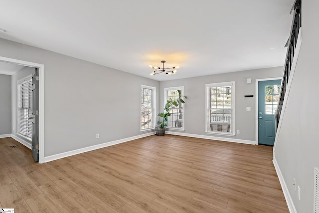 unfurnished room with an inviting chandelier, light hardwood / wood-style flooring, and a wealth of natural light