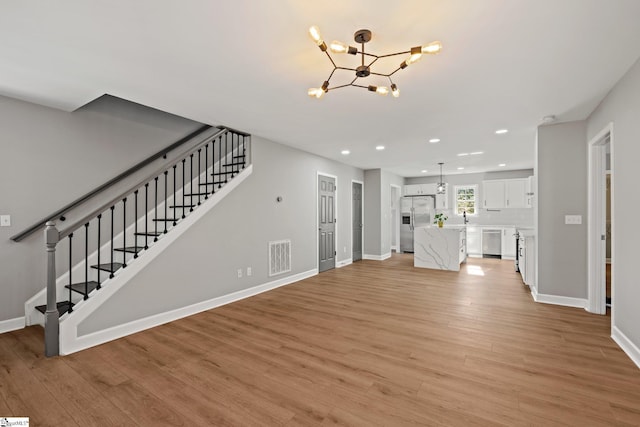 unfurnished living room featuring sink, a notable chandelier, and light hardwood / wood-style flooring