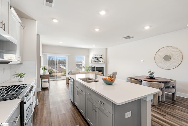 kitchen with stainless steel appliances, sink, decorative backsplash, dark hardwood / wood-style flooring, and a kitchen island with sink