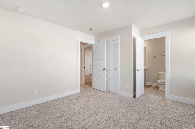 unfurnished bedroom featuring ensuite bathroom, a closet, and light carpet