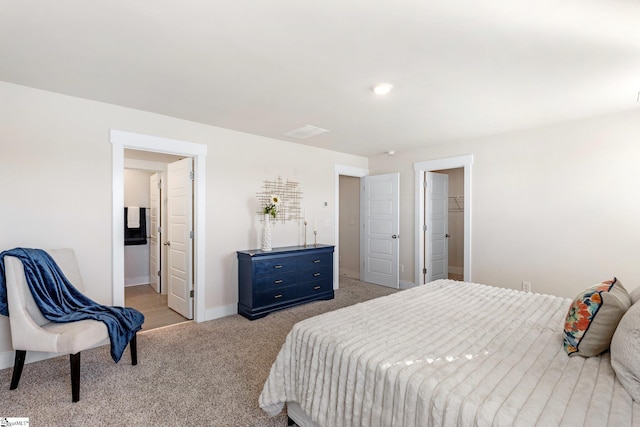 bedroom featuring a walk in closet, connected bathroom, and light carpet