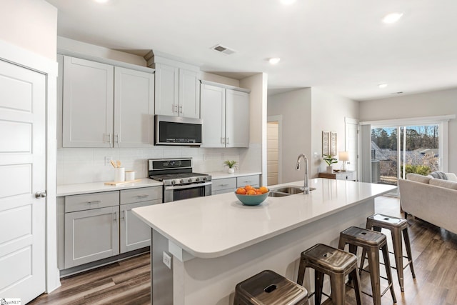 kitchen with sink, a center island with sink, dark hardwood / wood-style flooring, a breakfast bar, and appliances with stainless steel finishes