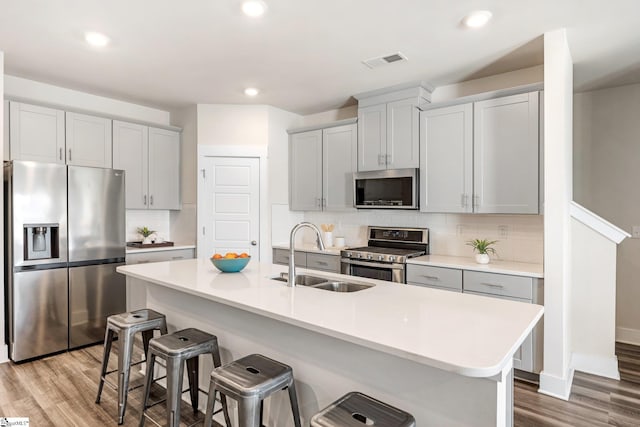 kitchen with sink, stainless steel appliances, light hardwood / wood-style flooring, and a center island with sink