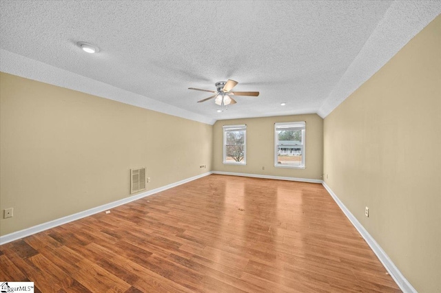 empty room with a textured ceiling, ceiling fan, light hardwood / wood-style floors, and vaulted ceiling