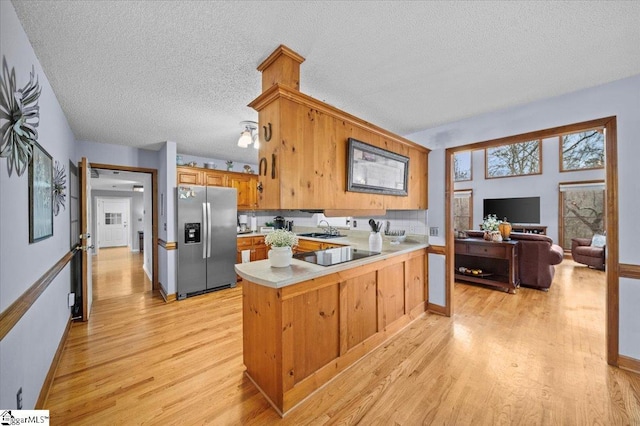 kitchen with a textured ceiling, stainless steel fridge with ice dispenser, light wood-type flooring, and kitchen peninsula