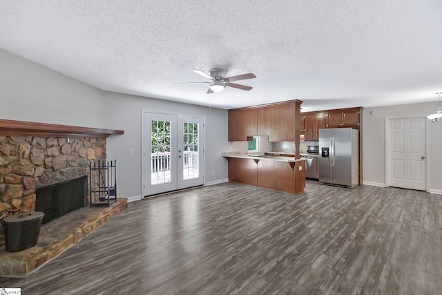 kitchen with a stone fireplace, stainless steel fridge with ice dispenser, kitchen peninsula, pendant lighting, and french doors