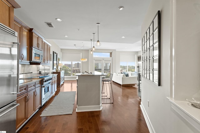 kitchen featuring dark wood-type flooring, pendant lighting, premium appliances, a kitchen bar, and a kitchen island