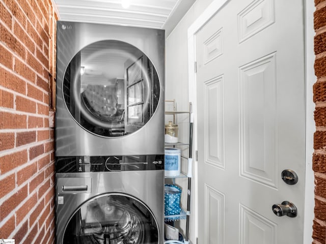 laundry area featuring brick wall and stacked washing maching and dryer