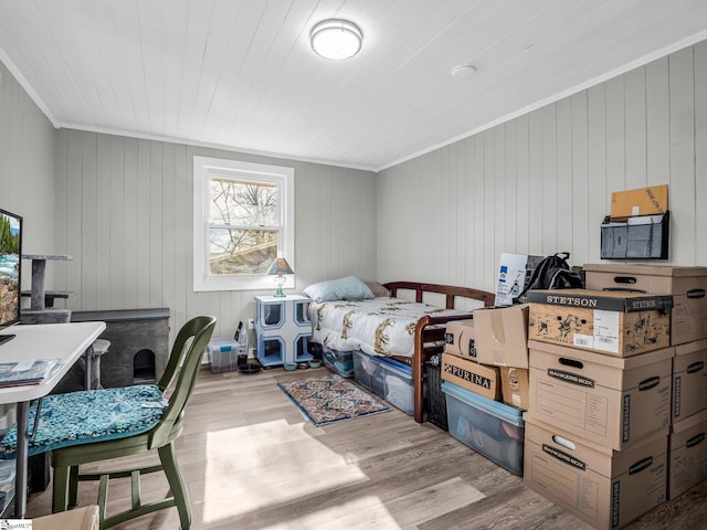 bedroom with light wood-type flooring, wooden walls, and crown molding