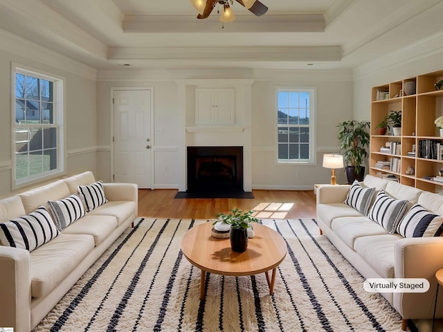 living room featuring light hardwood / wood-style floors, ceiling fan, a tray ceiling, and crown molding